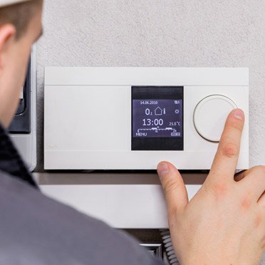 a heating technician in a grey shirt programming a heating thermostat of a heating system