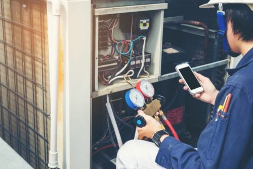 an HVAC technician in a blue shirt kneeling next to a HVAC unit on a HVAC service