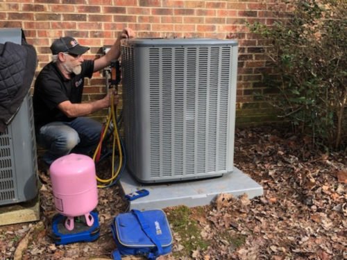 a hvac technician in a black shirt kneeling next to a HVAC unit in a backyard for an ac repair
